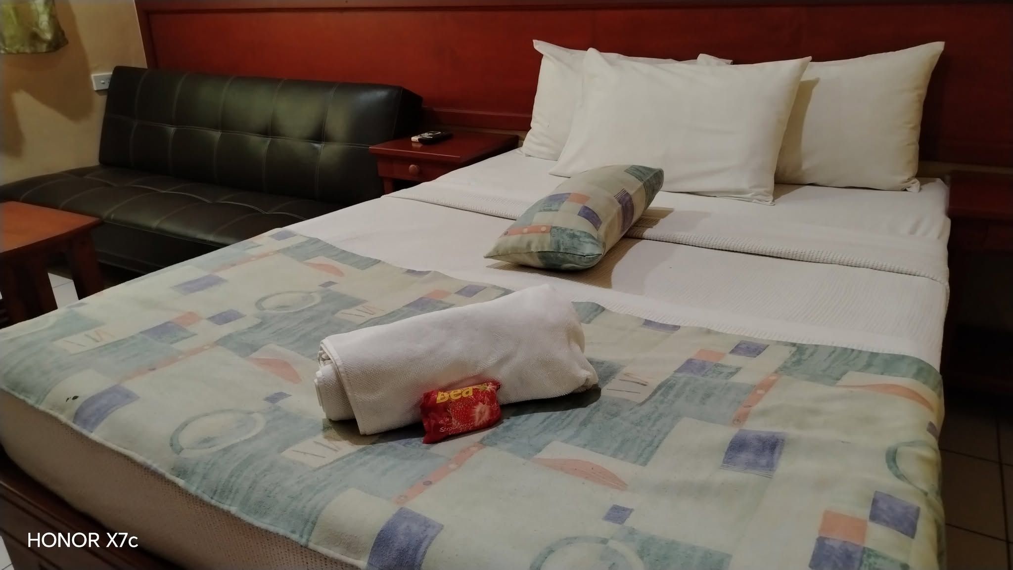 A double bed with fresh towels, a patterned throw, and a black leather sofa.