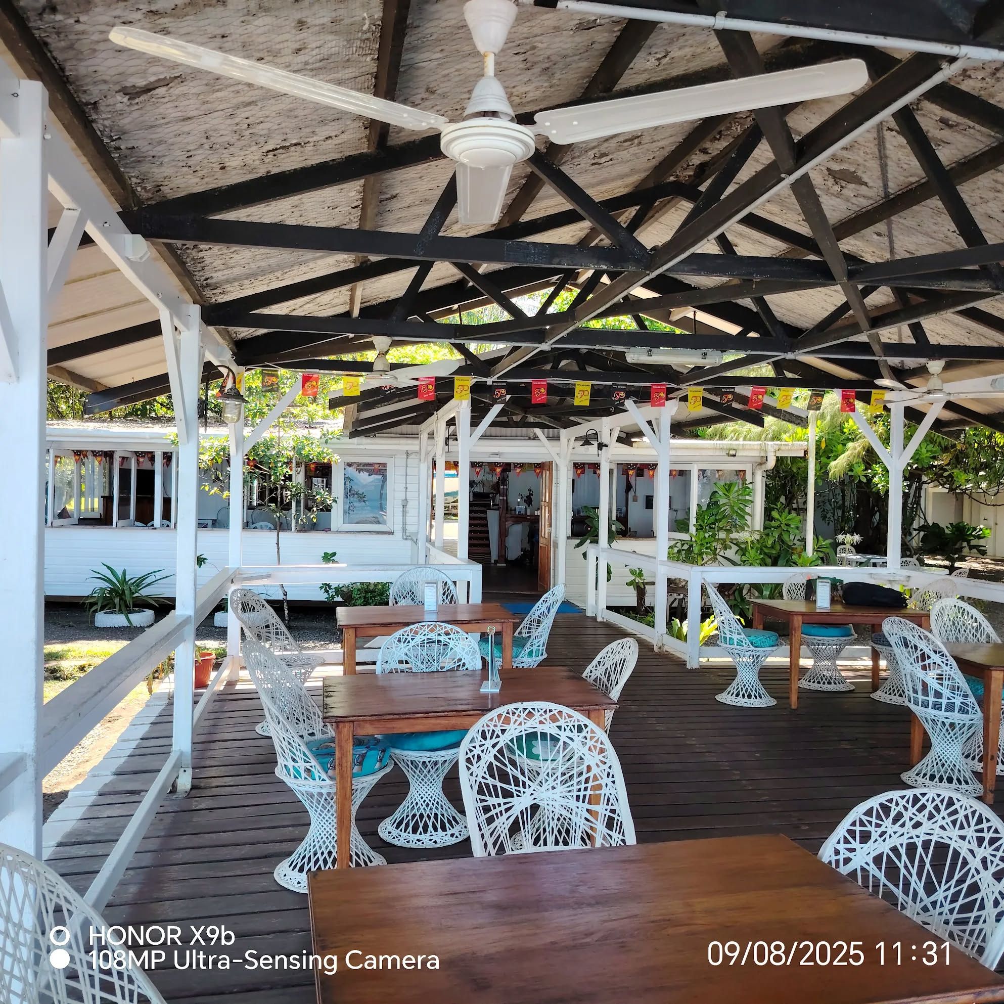 Open-air dining area with white wicker chairs and wooden tables under a canopy