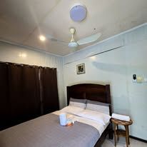 Double bed with white linens, side table, and wall-mounted fan.