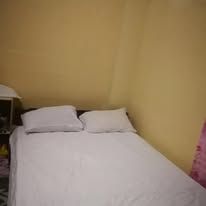 A neatly made double bed with two pillows against a yellow wall.