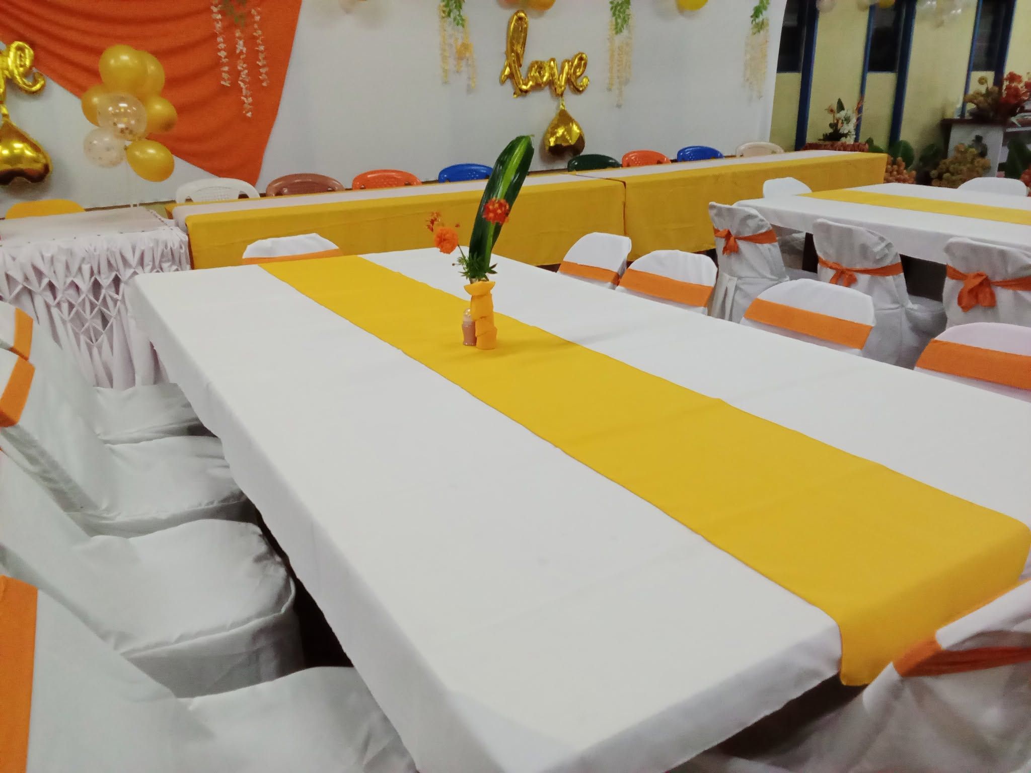 Event dining setup with white tablecloths and orange decorative runners.