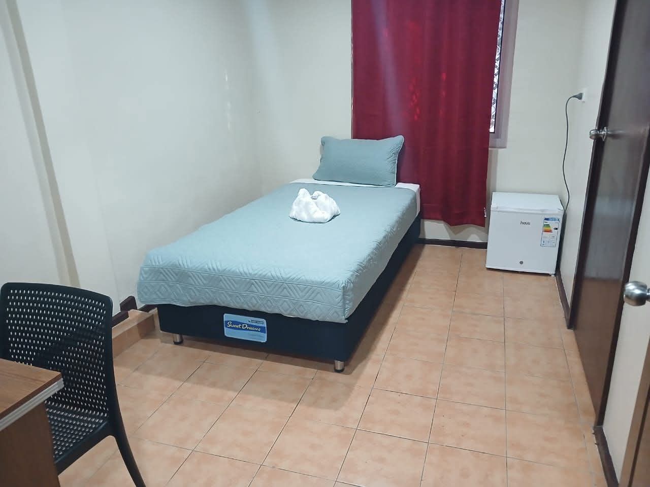 Single bed with blue linens and a small bedside refrigerator