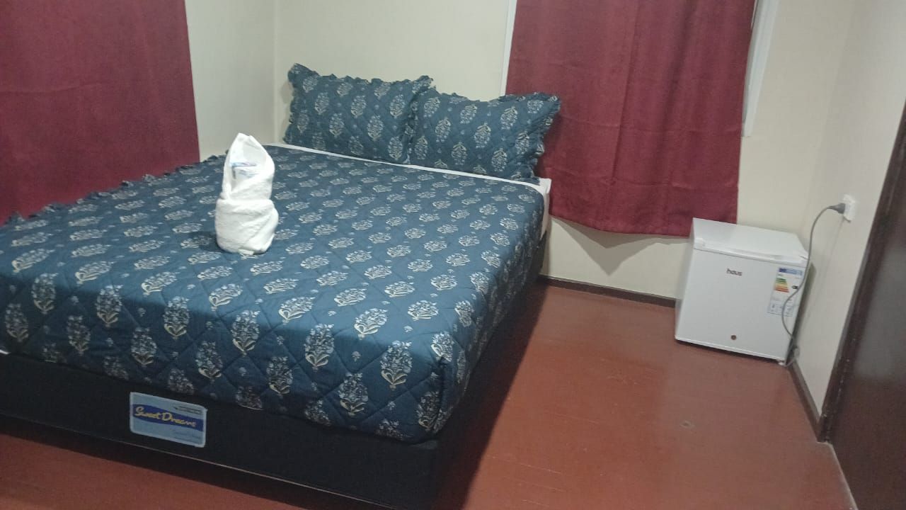 Double bed with patterned blue bedding and a white compact fridge