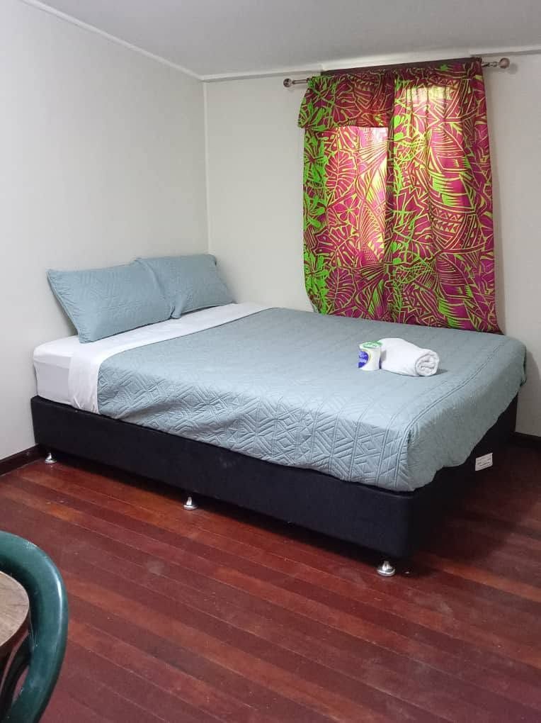 Bedroom with hardwood floors, a single bed, and patterned green and pink curtains.