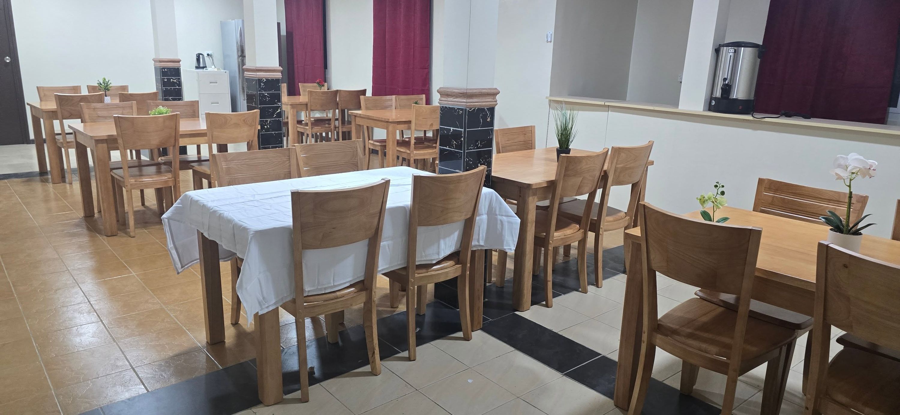 Spacious dining area with multiple wooden tables, chairs, and tiled floors.