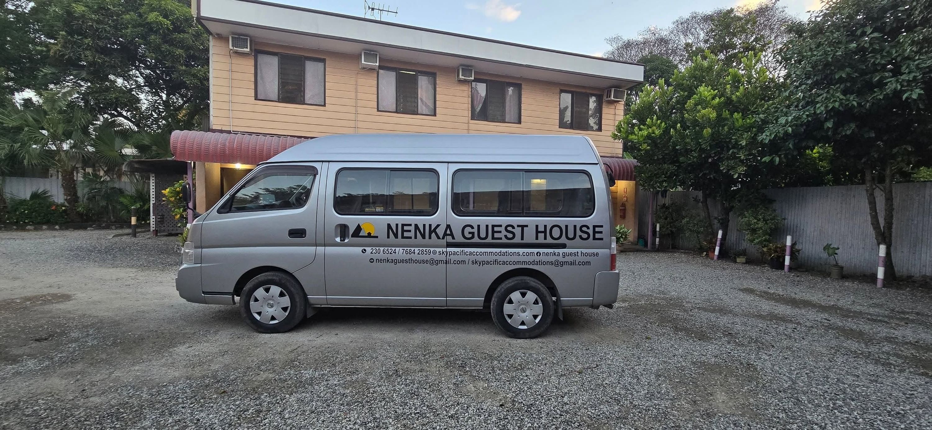 Guest house shuttle van parked in the gravel driveway in front of the building.