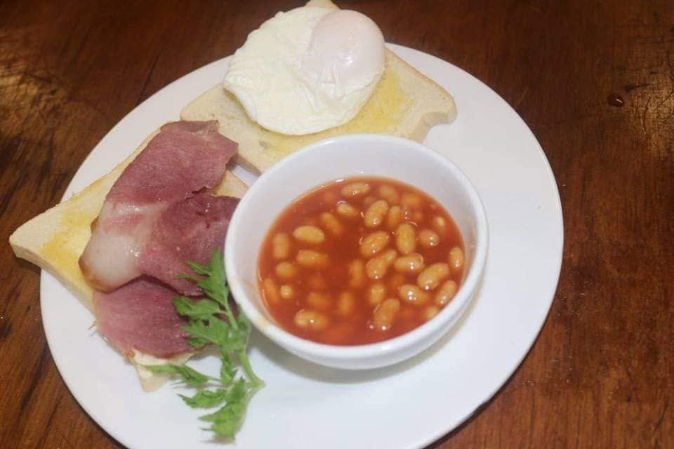 Breakfast plate with poached egg on toast, bacon, and baked beans.