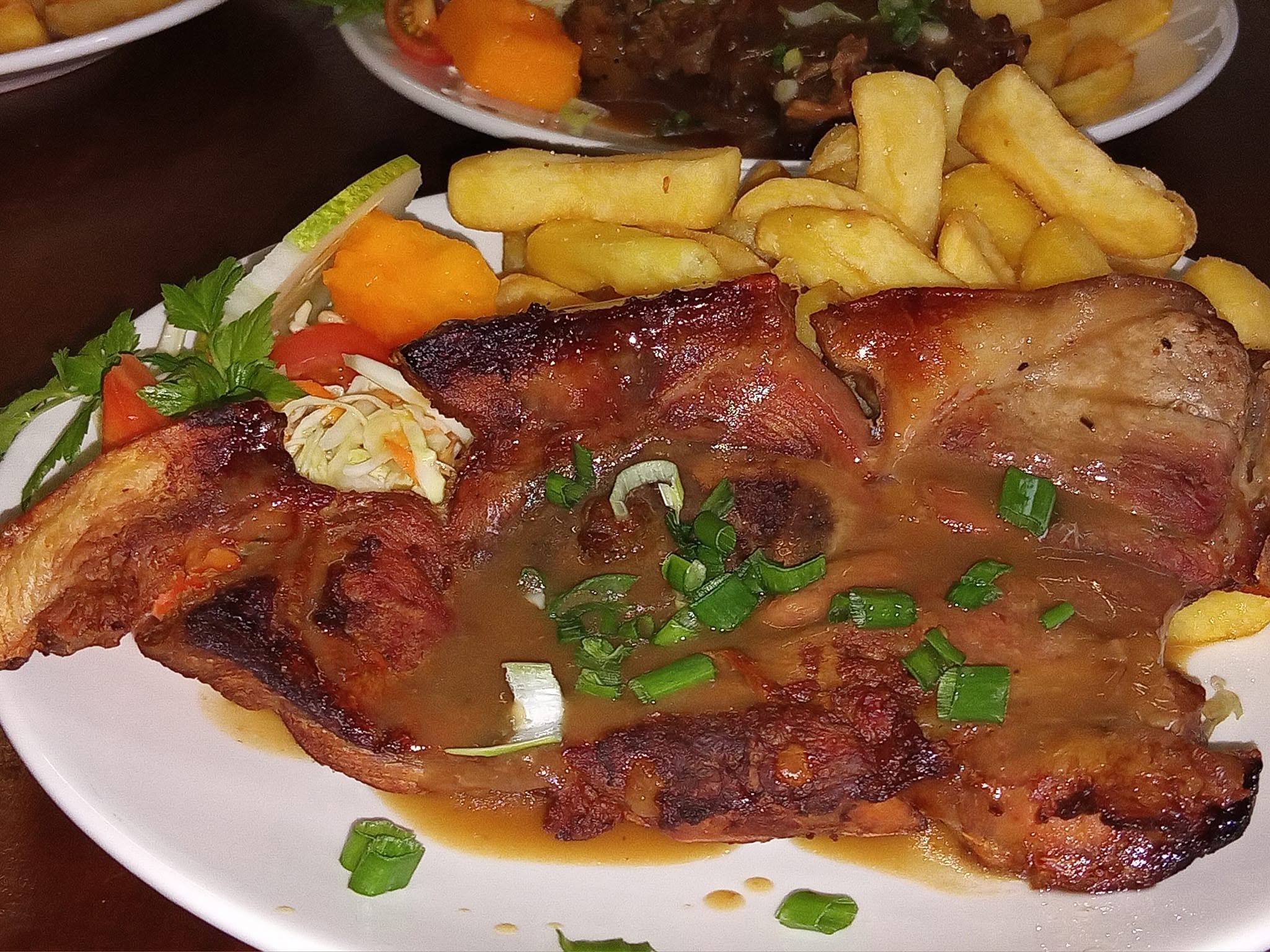 Grilled t-bone steak with gravy, fries, and a side of vegetables.