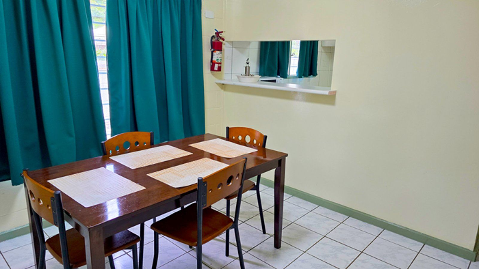 Wooden dining table with four chairs and green curtains.