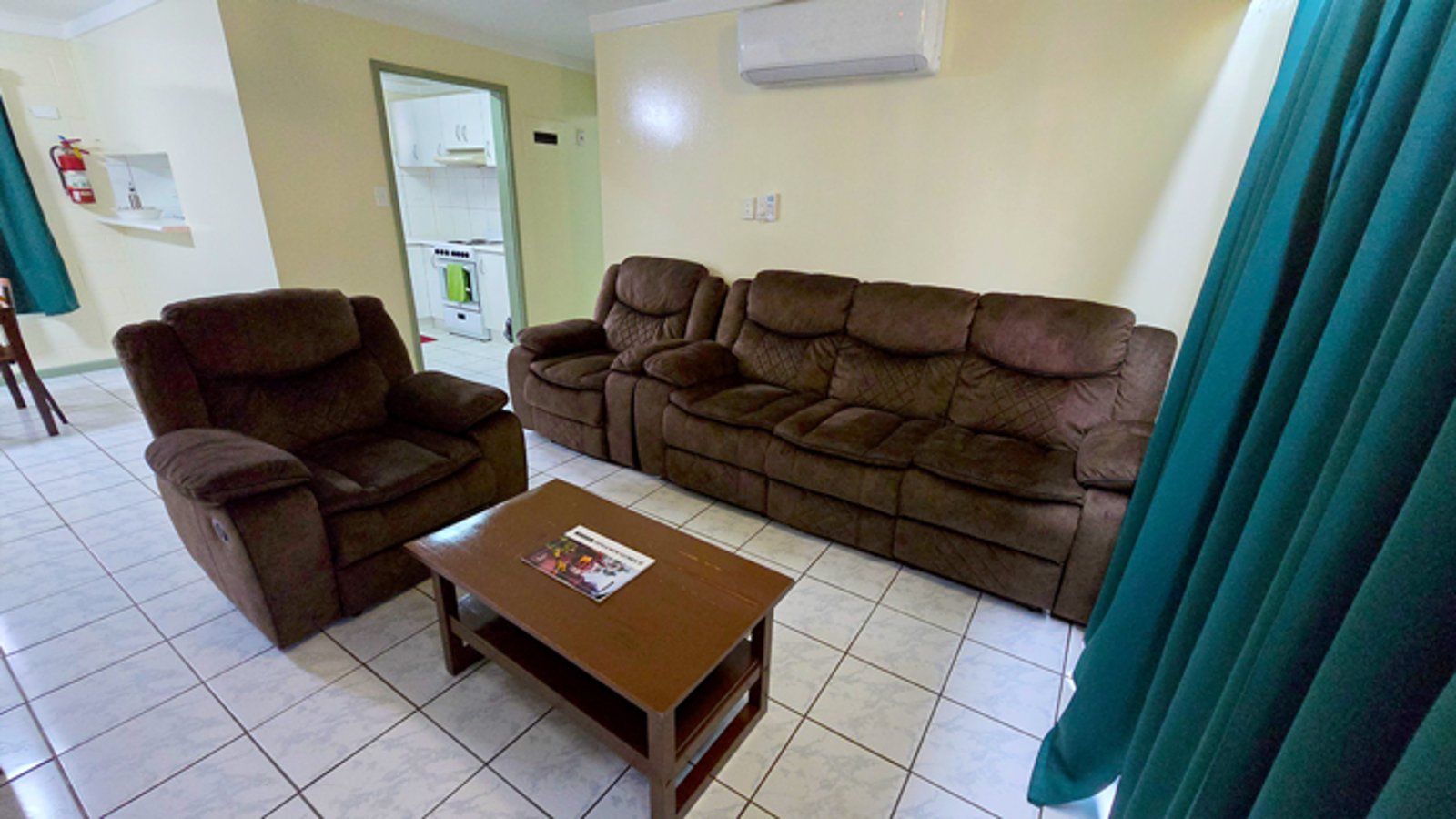 Spacious living room with air conditioning, comfortable seating, and tiled floors.