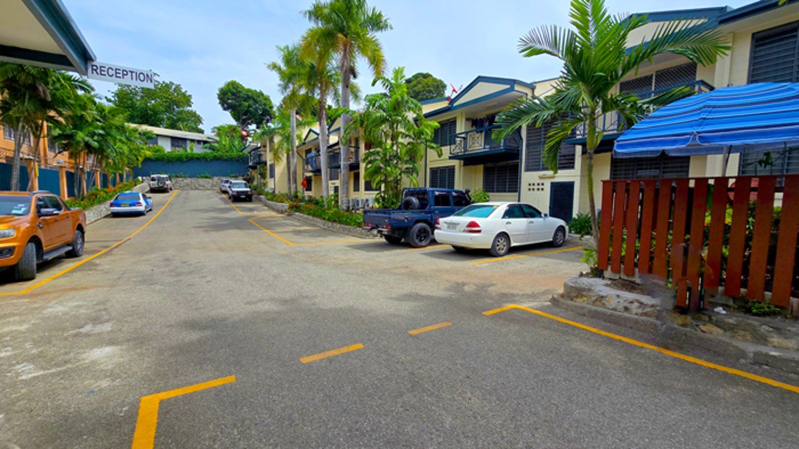 Paved parking area leading to the reception entrance with palm trees.