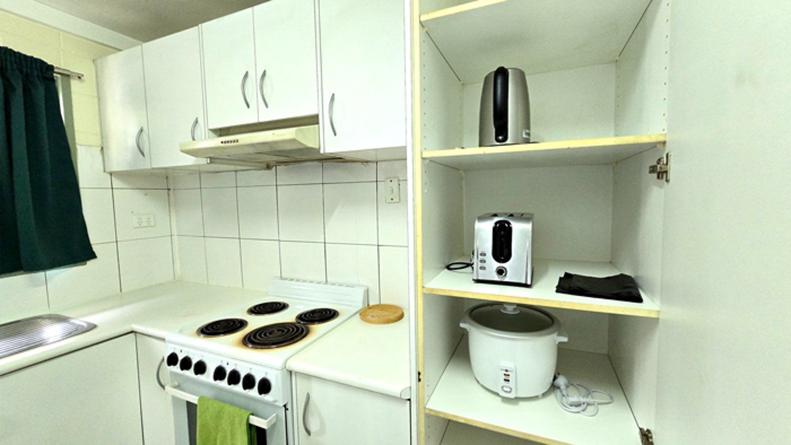 Kitchen space with a white electric stove, kettle, toaster, and rice cooker.