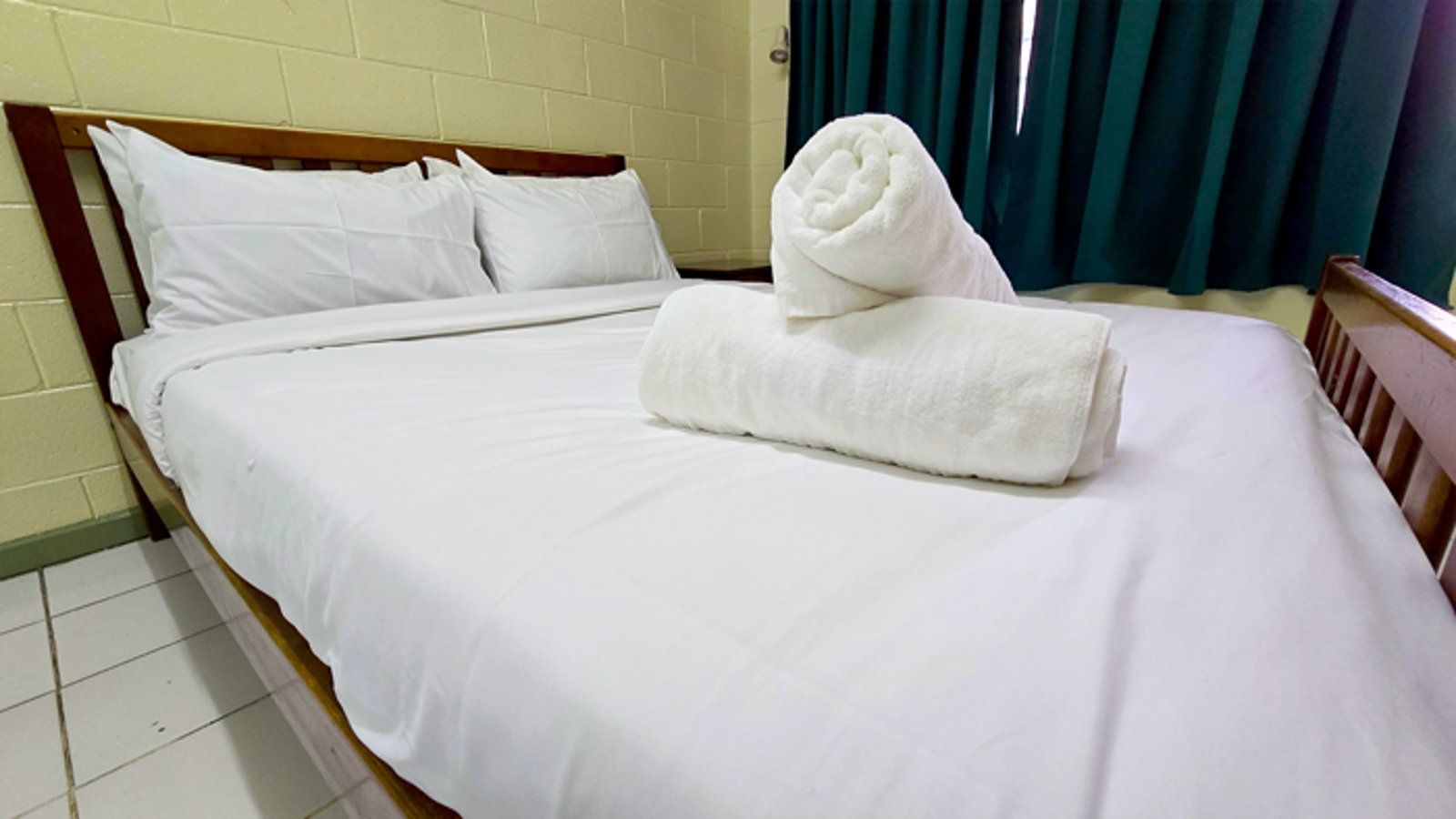Double bed with white linens and rolled towels against a block wall.