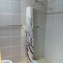 Ensuite shower area with grey floor-to-ceiling tiles and printed curtain.