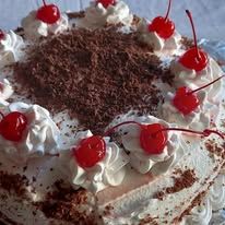 Cream cake topped with shaved chocolate and multiple glacé cherries.