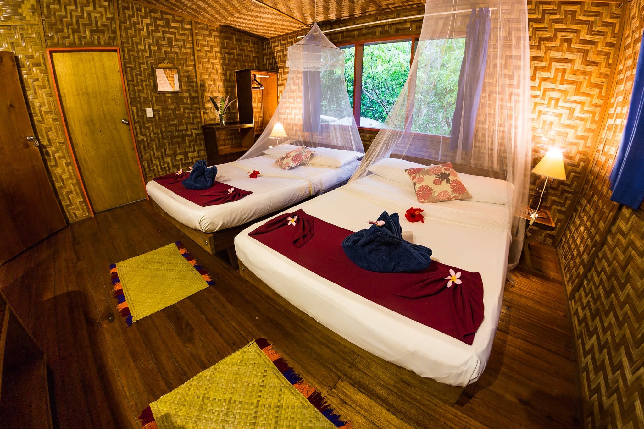 Traditional island style bedroom with two beds, mosquito nets, and woven walls.