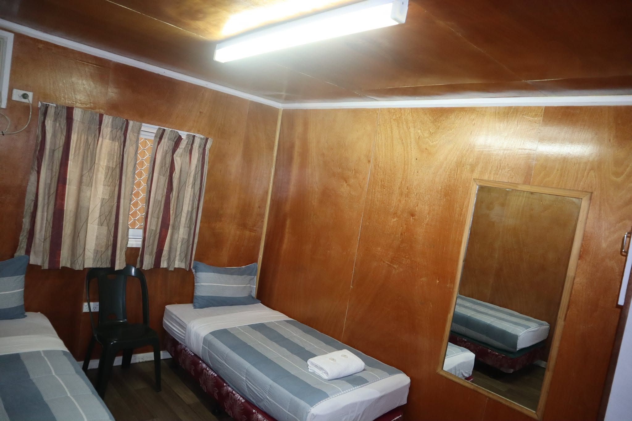 Twin bedroom featuring wood-paneled walls, single beds, and a large wall mirror.