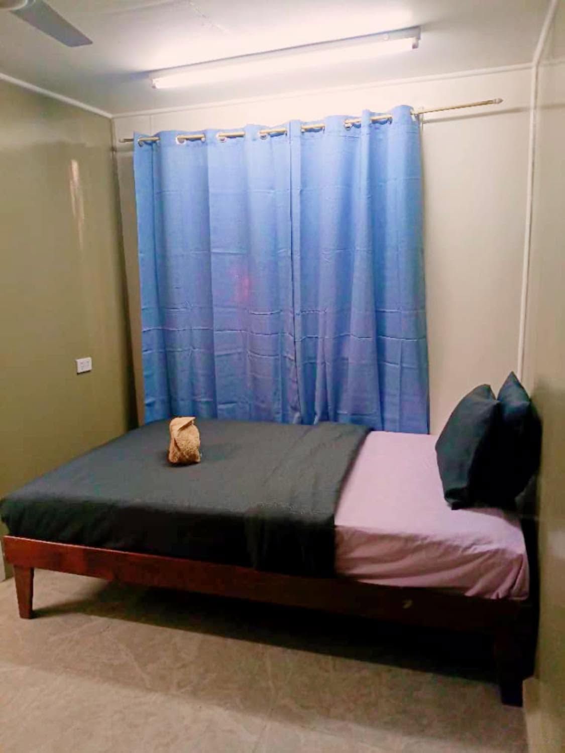 Single bed with dark linens and blue window curtains in a guest room.