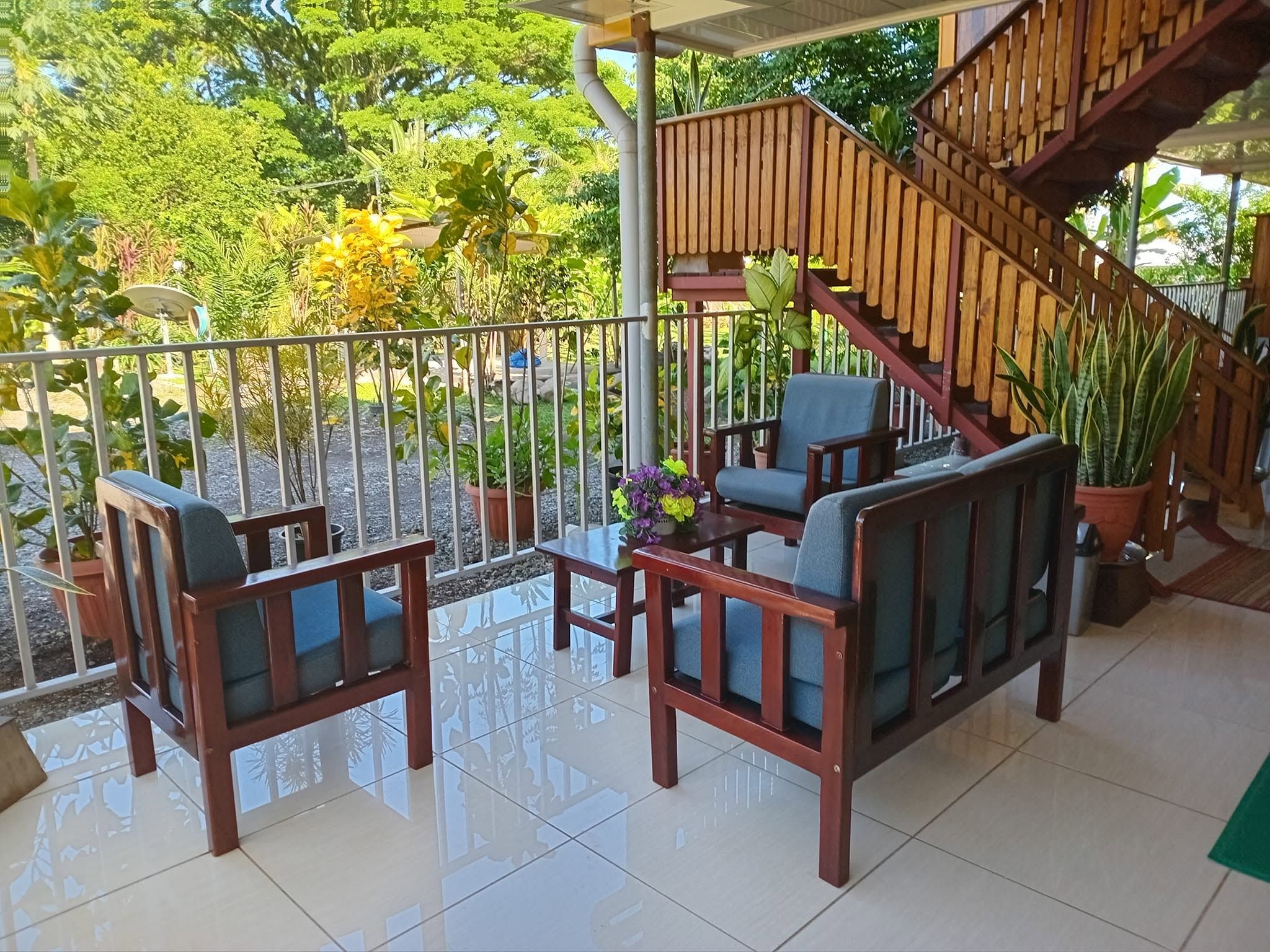 Outdoor tiled patio seating area with wooden armchairs and garden view