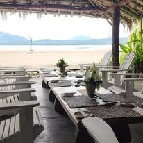 Open-air beachfront dining area with white wooden chairs and sea view.