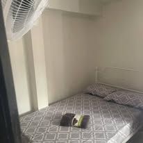 Simple guest room featuring a double bed with patterned linens and wall fan.
