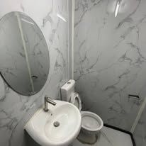 Compact bathroom with white marble-patterned walls, pedestal sink, and mirror.
