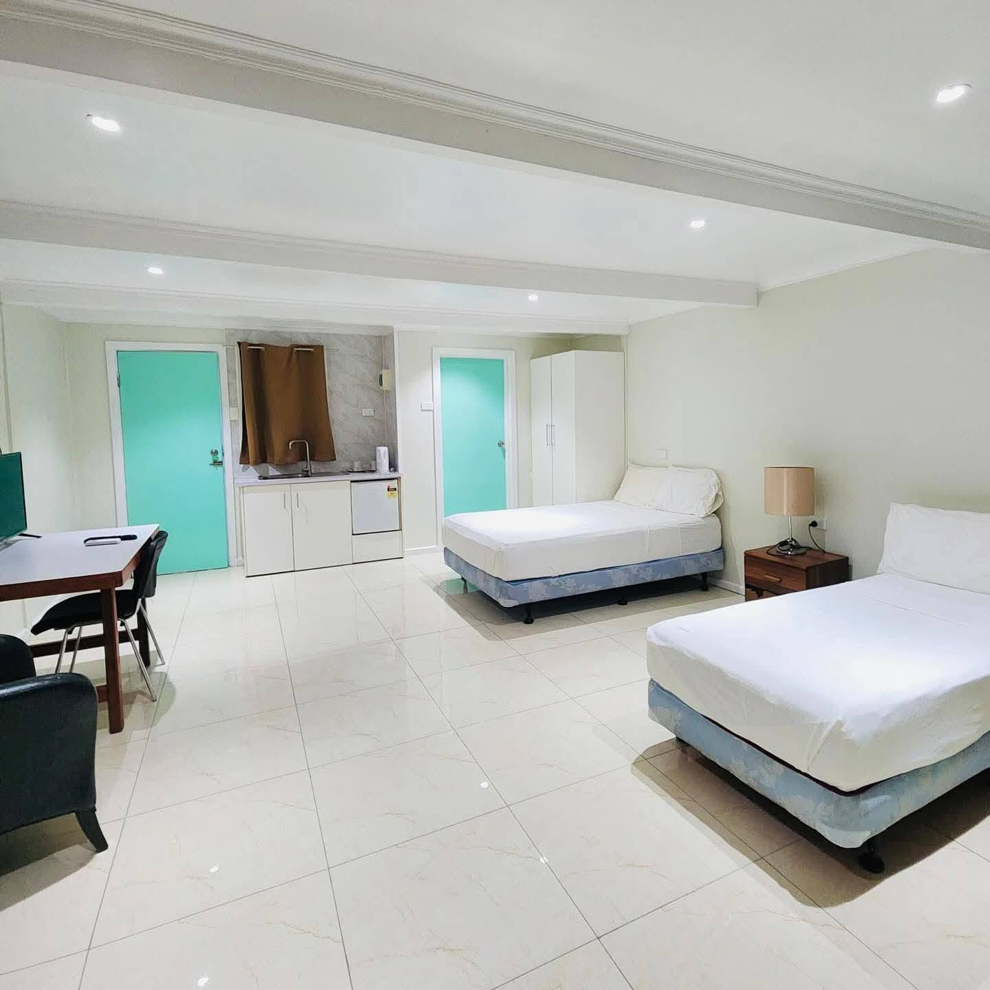 Spacious tiled guest room featuring twin beds, desk area, and kitchenette facilities.