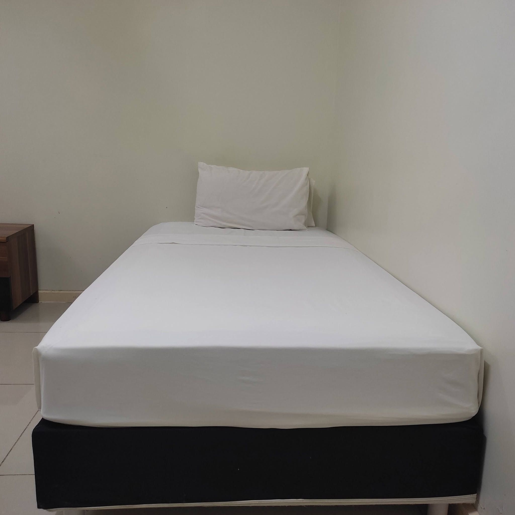 Single bed with white linens and bedside table in a clean, minimalist setting.