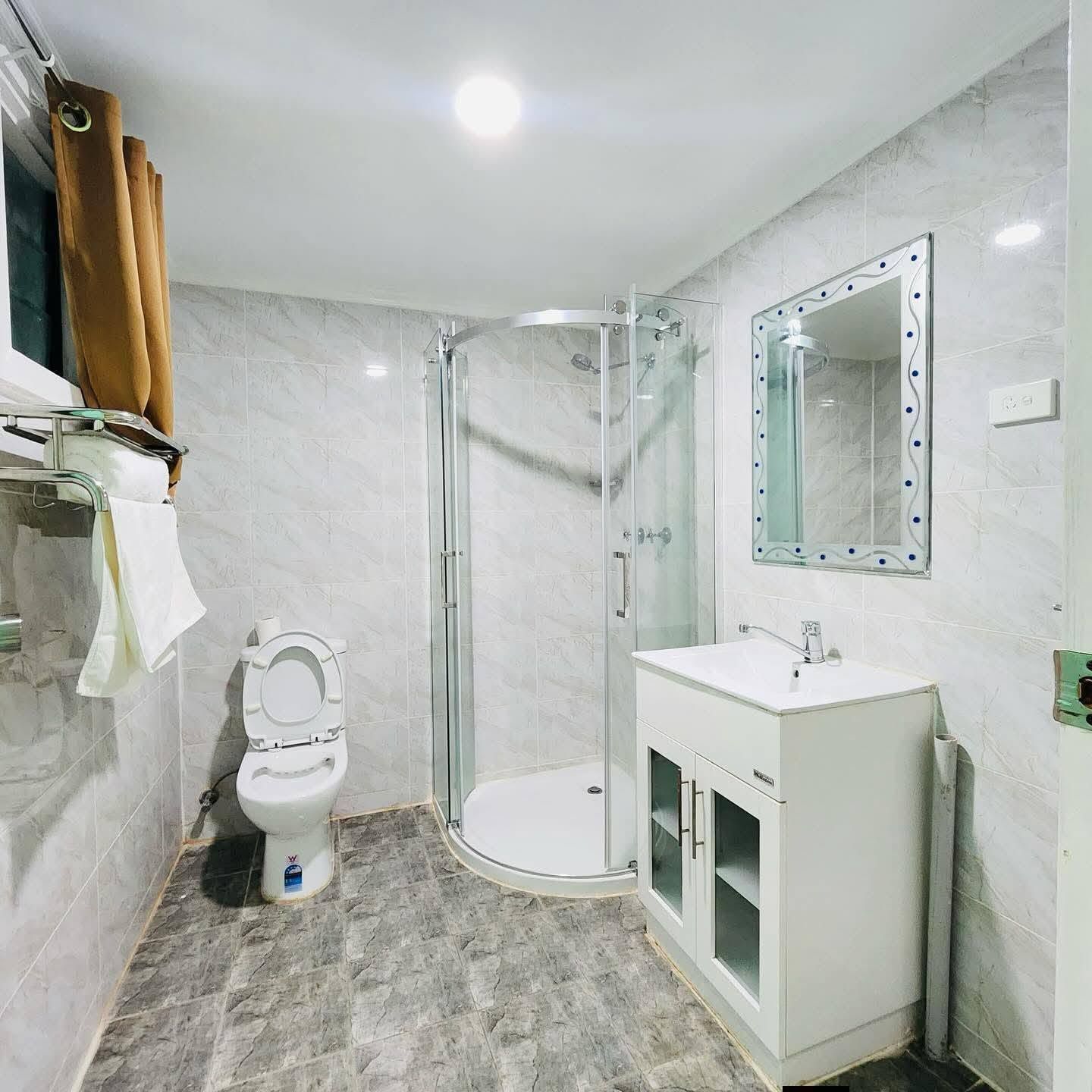 Bathroom featuring a curved glass shower stall, white vanity, and toilet.