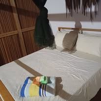 A tidy double bed with white linens and a mosquito net in a wood-paneled room.