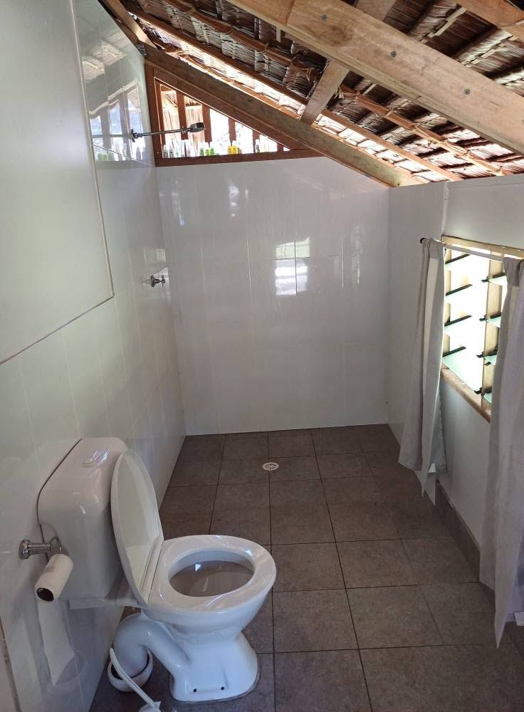 Tiled bathroom featuring a toilet and shower under a sloped thatched ceiling.