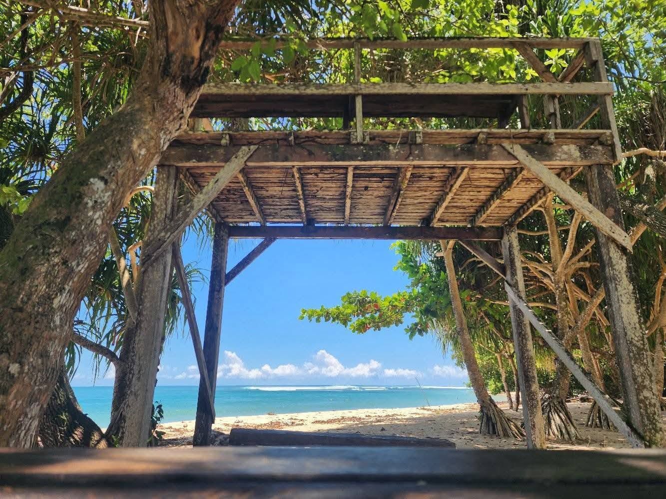 Ocean views through a rustic wooden structure on the sandy beachfront.