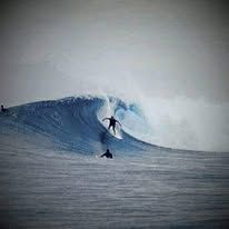 A surfer riding a large breaking wave in the ocean near the lodge.