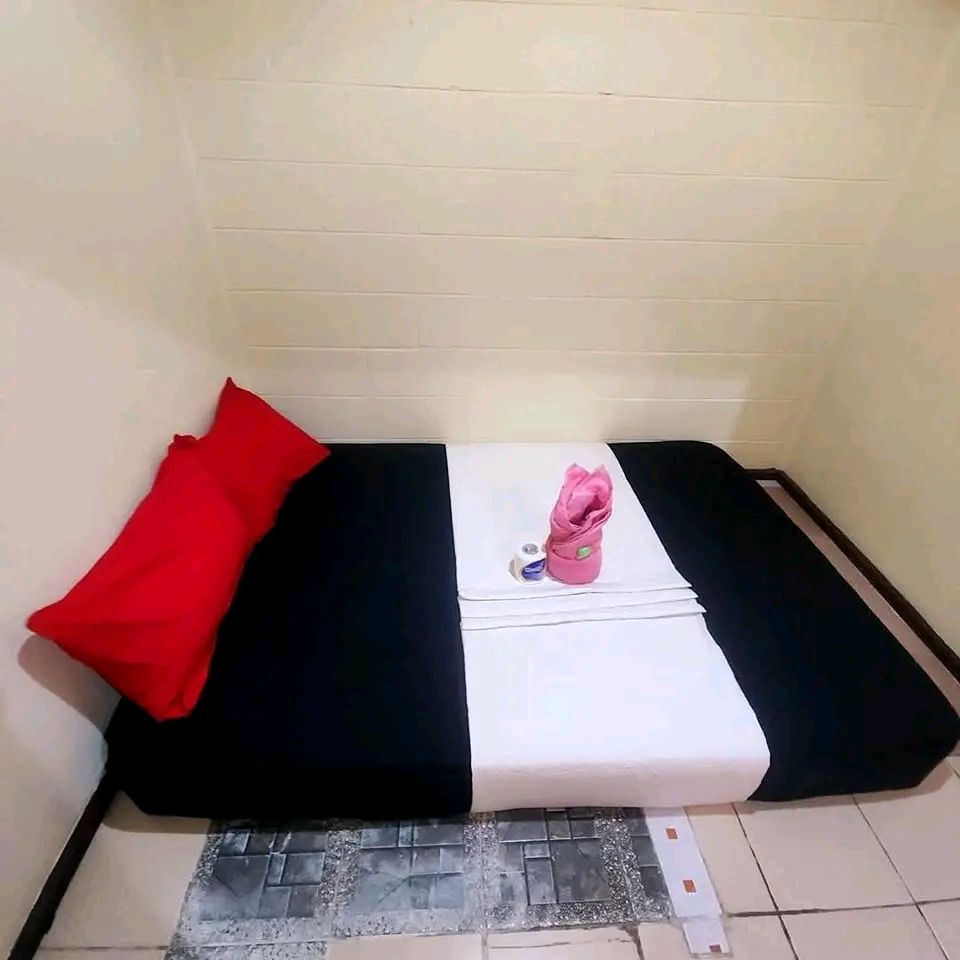 Single bed with black sheets, red pillows, and folded pink towel.