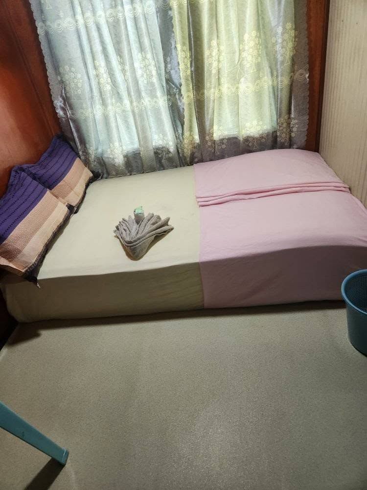 Compact guest room featuring a bed with pink linens and draped curtains.