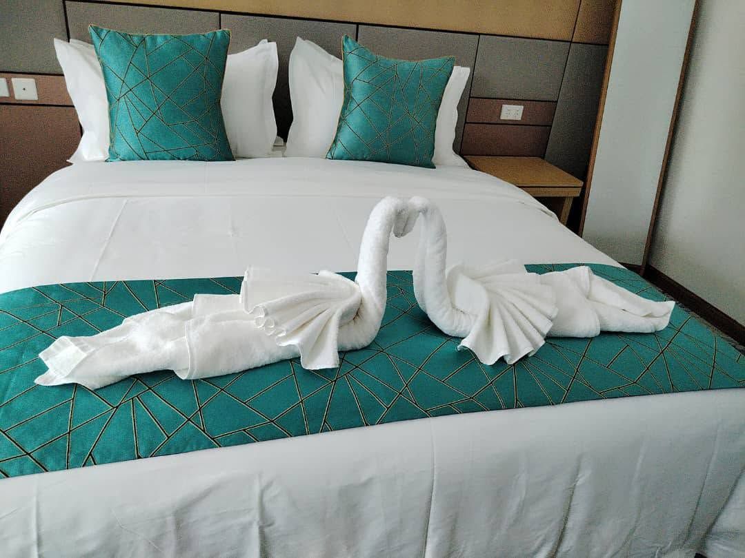 Double bed with decorative teal pillows and towel art swan arrangement.