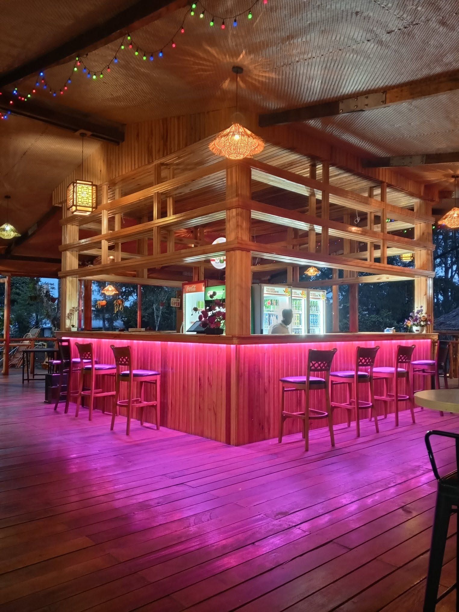 Outdoor wooden bar area with pink ambient lighting and bar stool seating.