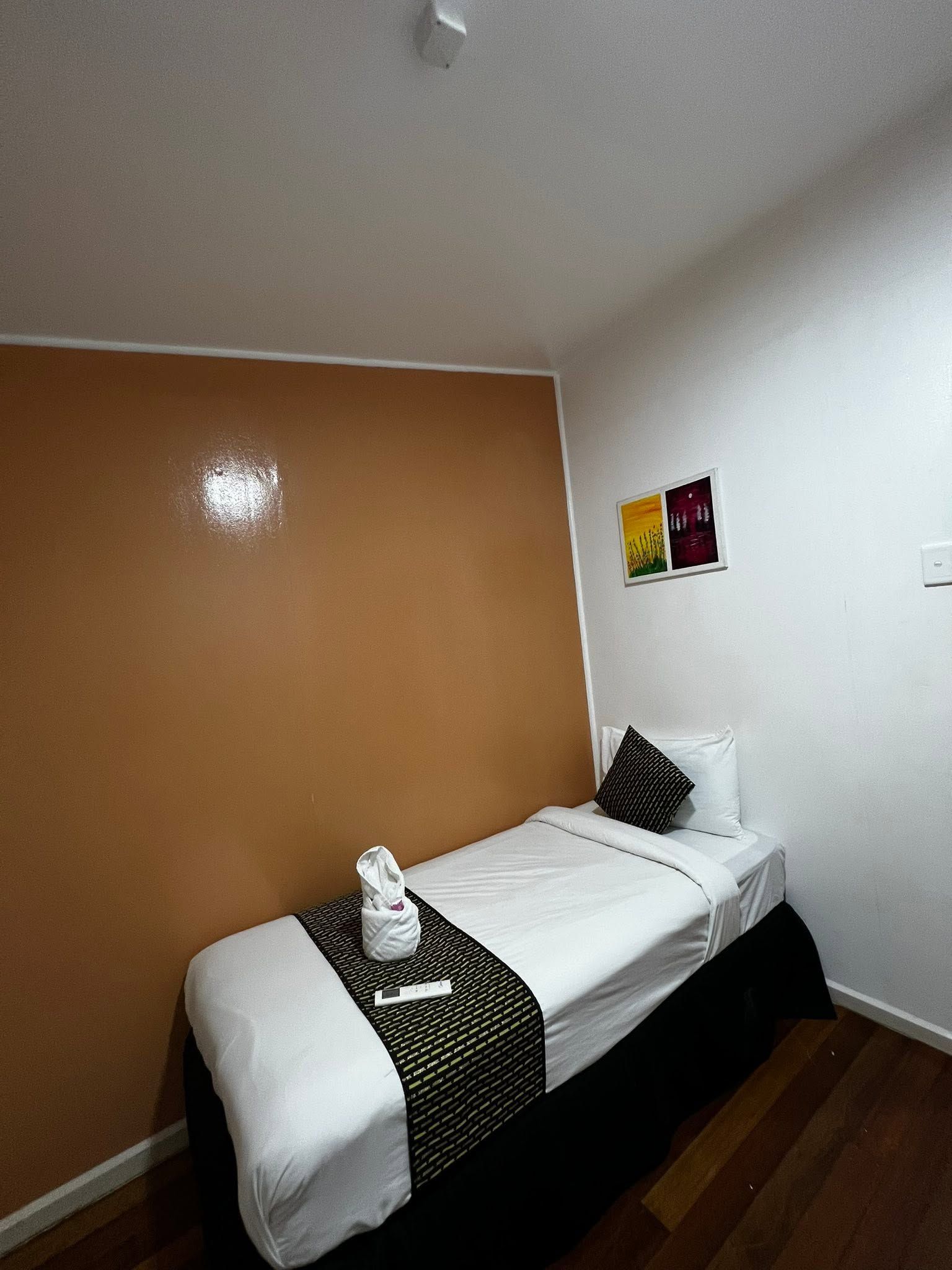 Small single bed with white linens and a decorative brown runner in a corner nook.