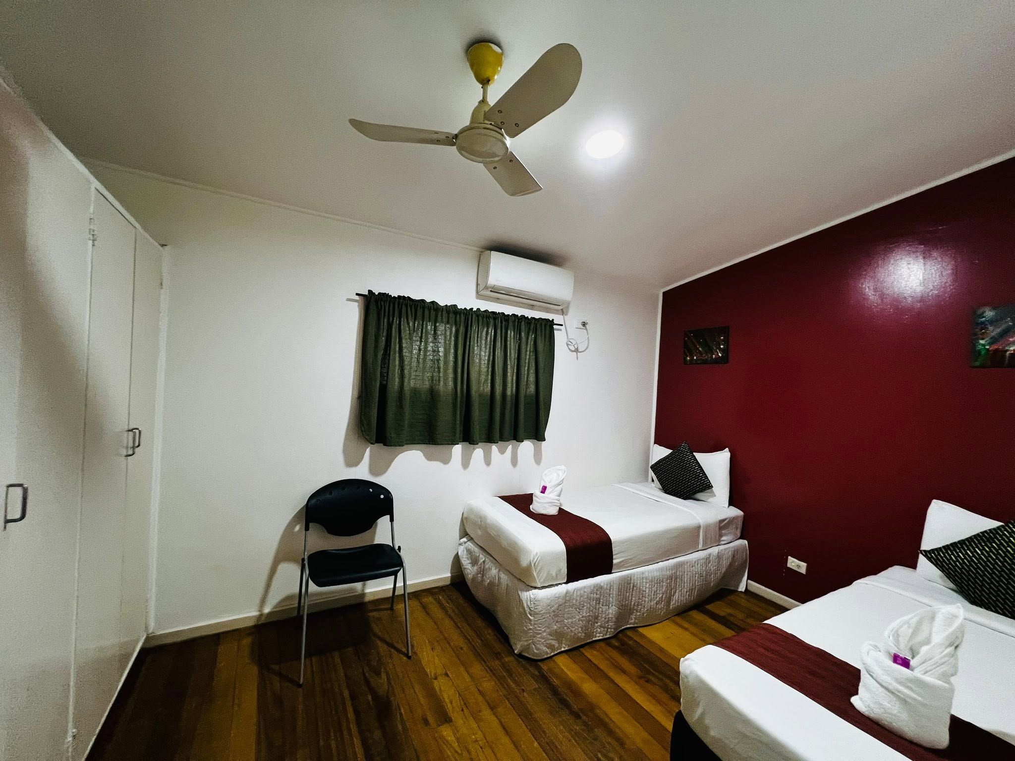 Twin bedroom features wooden floors, a ceiling fan, and a deep red accent wall.