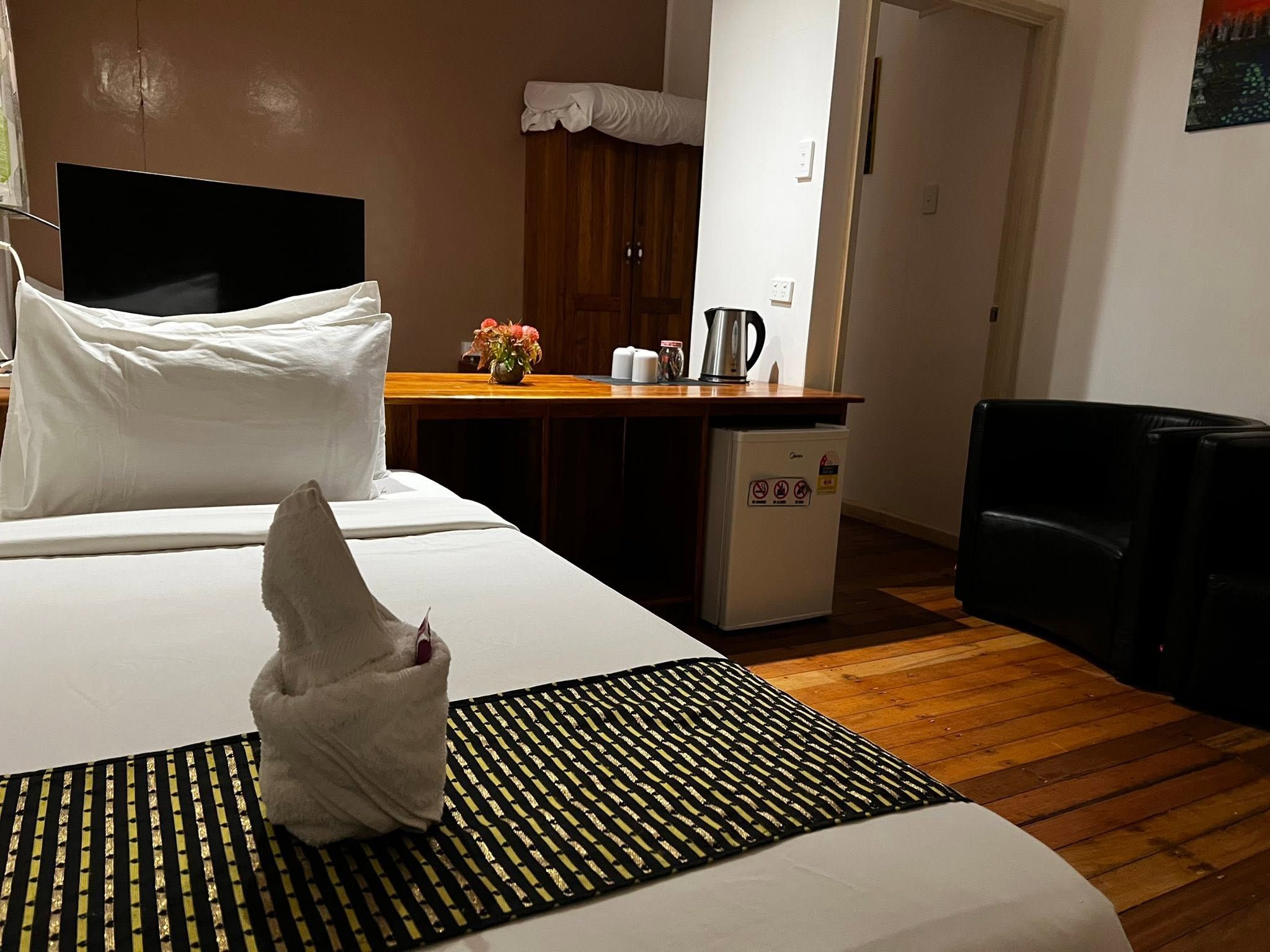 Guest room interior featuring a double bed, wooden desk, mini-fridge, and kettle.