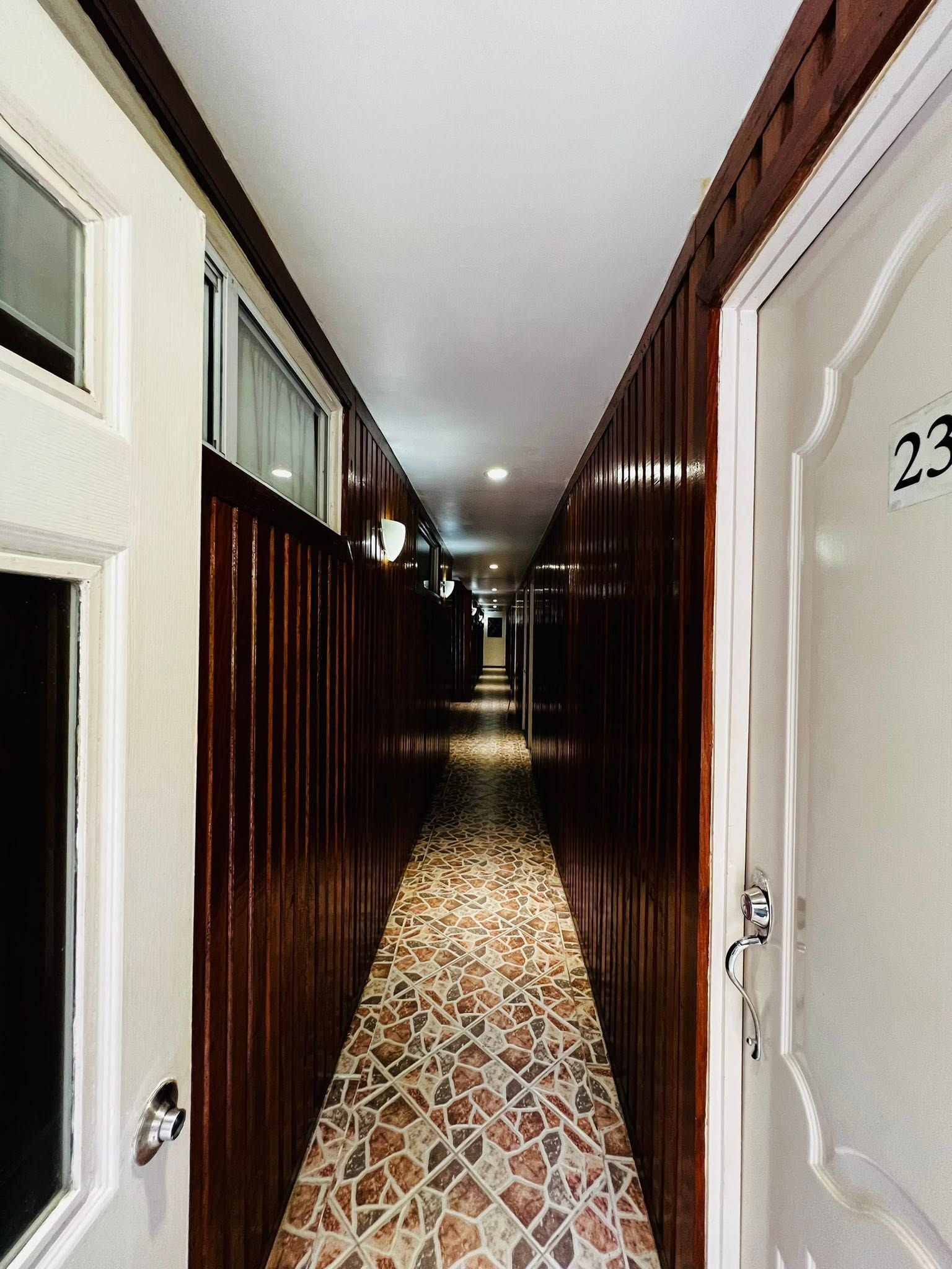 Narrow interior hallway with dark wood-paneled walls and mosaic stone tile flooring.