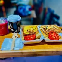 Breakfast takeaway trays with french toast, tomatoes, and a hot beverage.