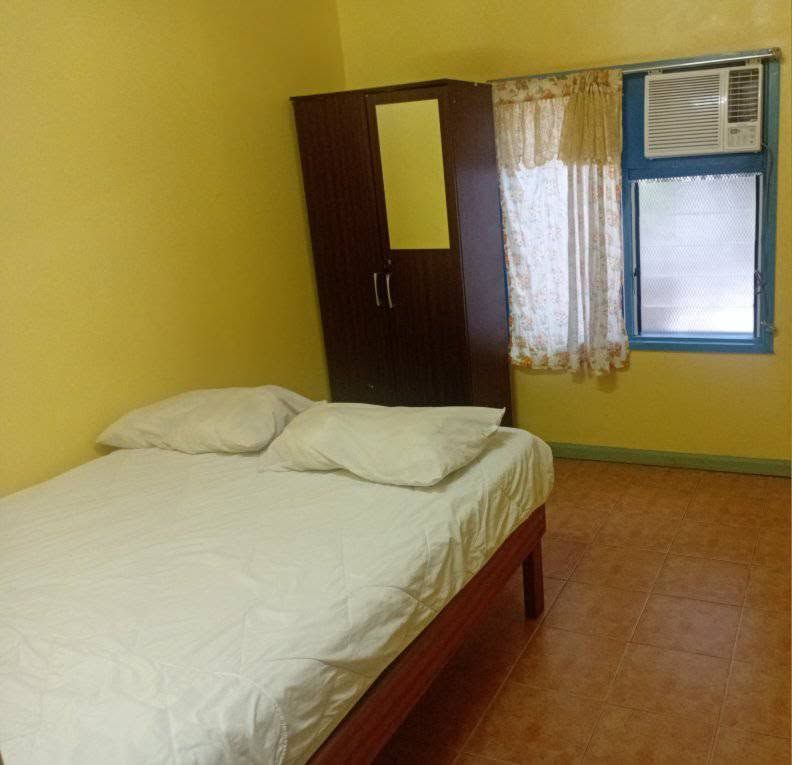 A double bed with white linens next to a wooden wardrobe and window unit.