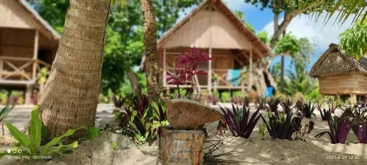 Traditional thatched-roof bungalows set on a sandy beach landscape.