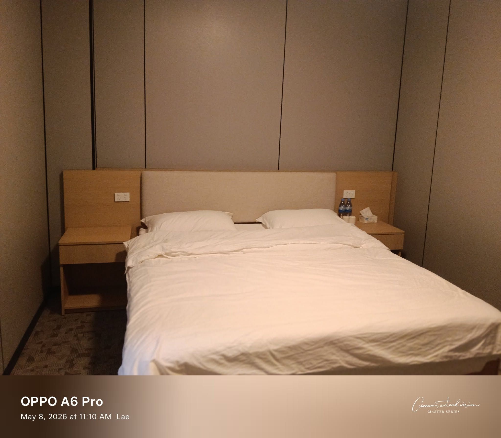 Single large bed with light wood headboard and built-in side tables.