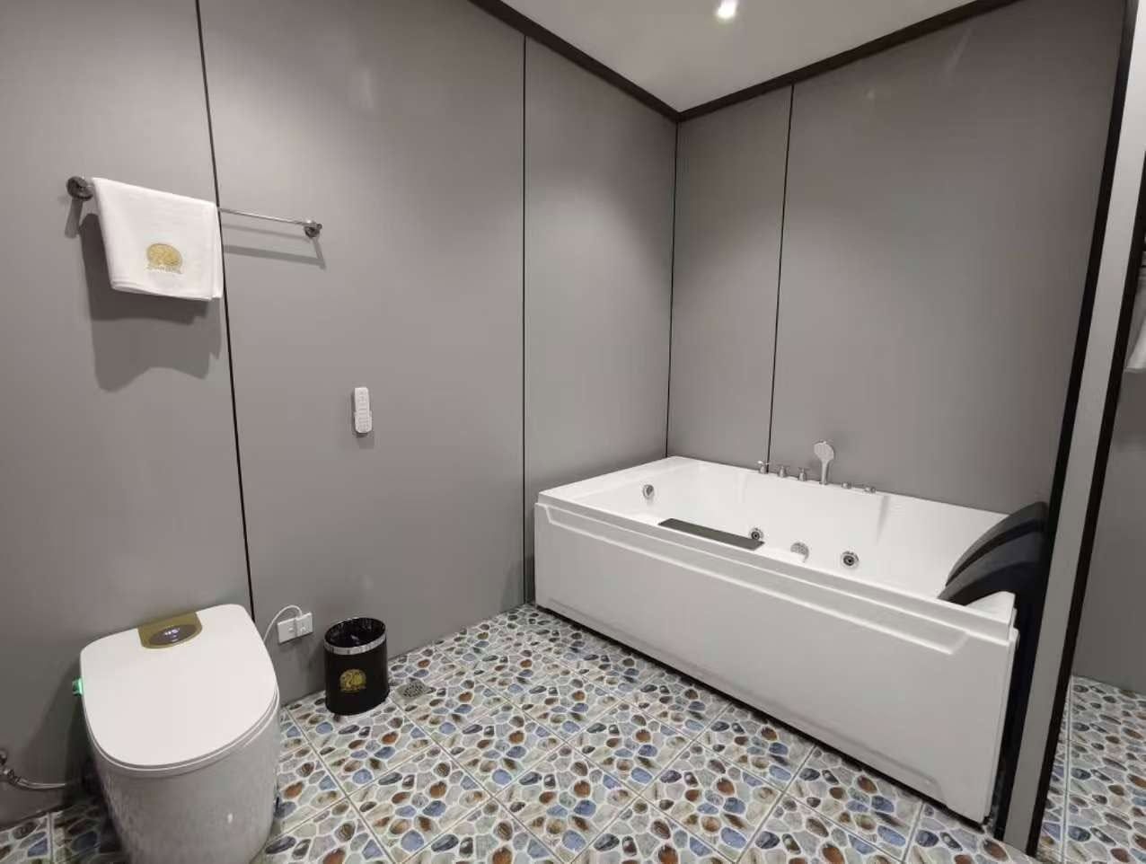 Large white soaking bathtub and modern toilet with pebble-patterned floor tiles.