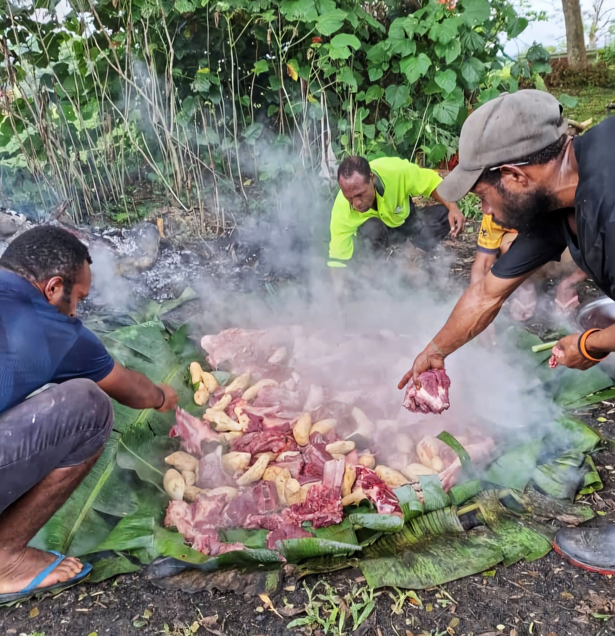 Traditional mumu cooking preparation with meat and vegetables on banana leaves.