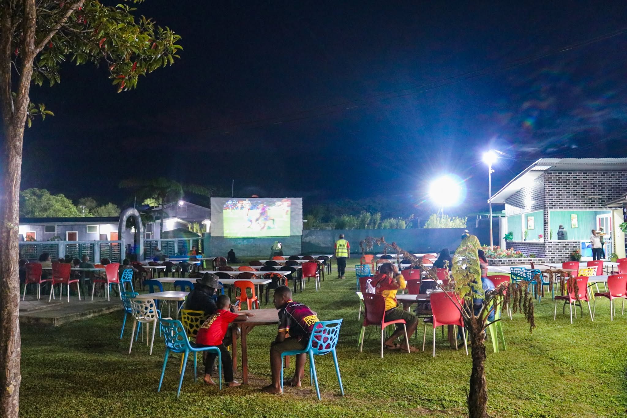 Outdoor cinema setup showing sport on a large screen at night