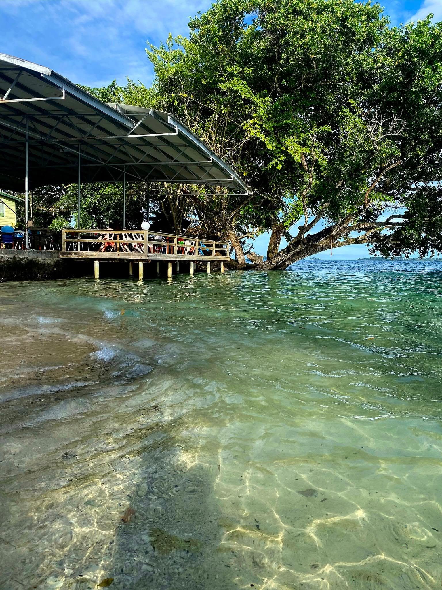 The resort's beachfront dining deck shaded by a large tree.