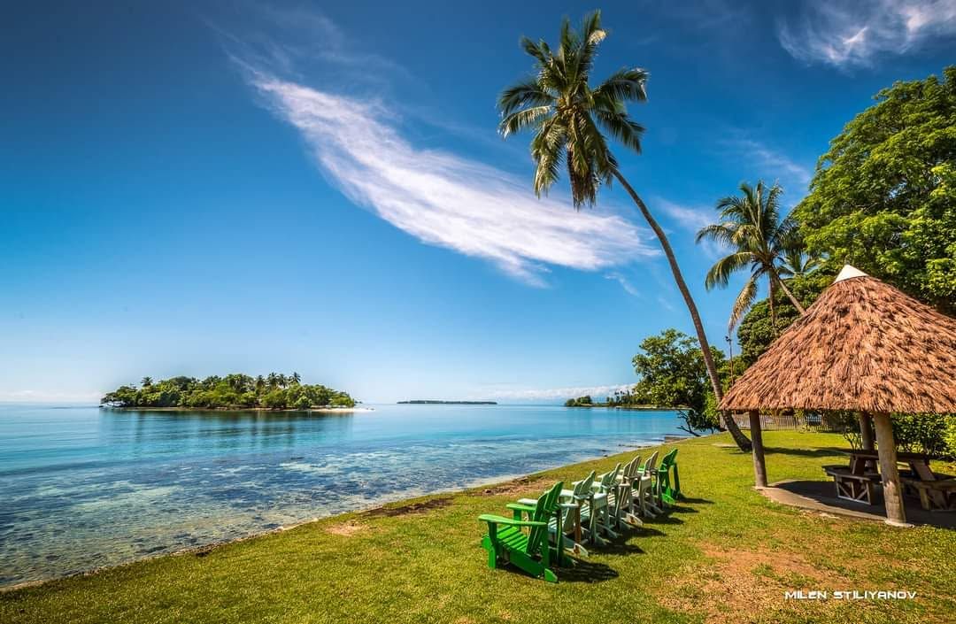 Green lawn chairs and a thatched-roof pavilion by the shoreline.
